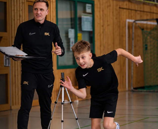 Ein junger Fußballer startet neben einer Lichtschranke, während Stefan Kehrer die Sprintmessung begleitet